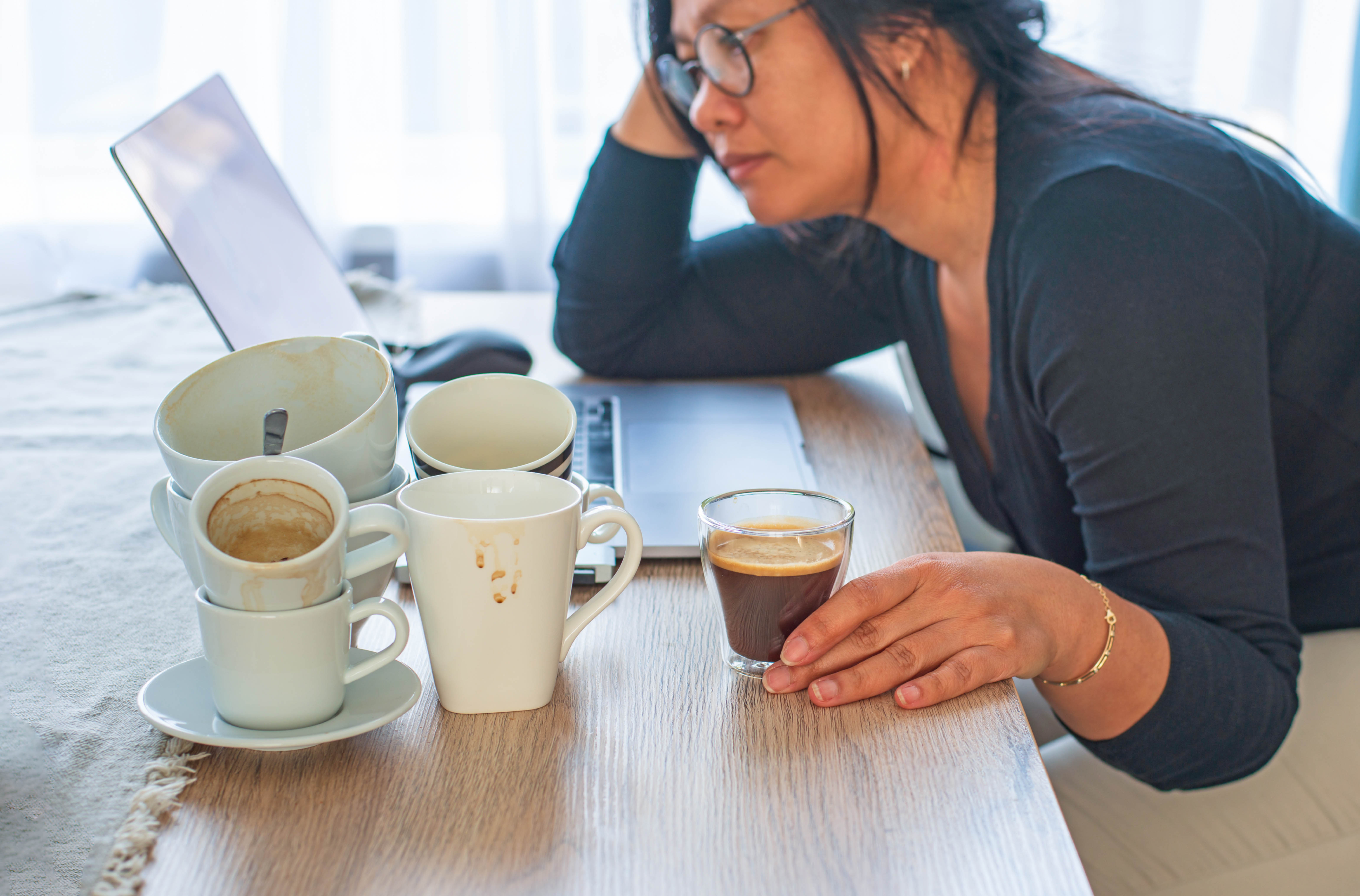 Woman at her laptop surrounded by empty coffee cups and an espresso